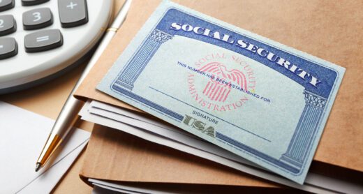 A Social Security card rests on top of a stack of file folders and next to a calculator and a pen.