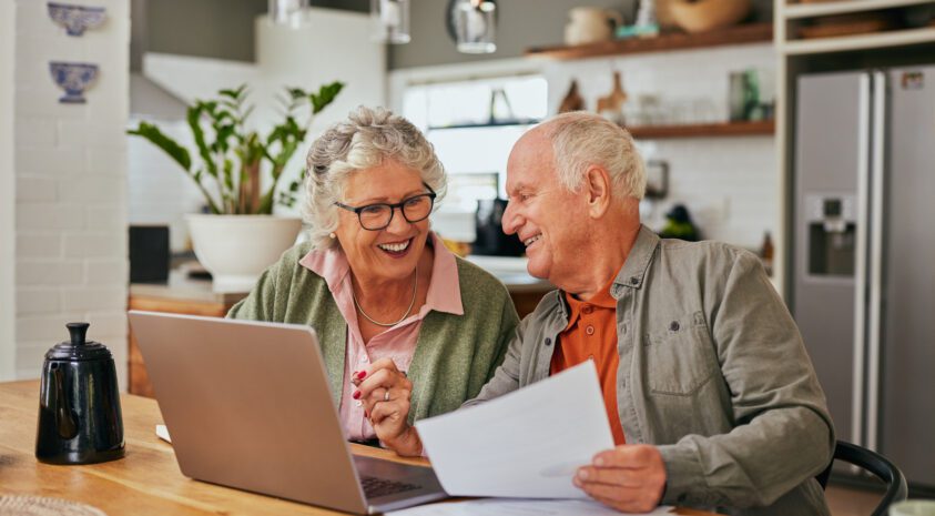 Happy retired couple works on their taxes at their kitchen table.