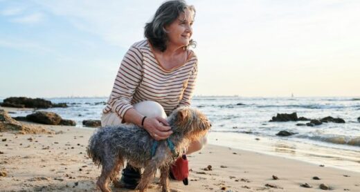 Older woman crouching with her dog at the beach.
