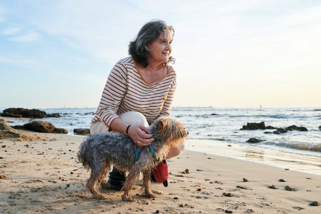 Older woman crouching with her dog at the beach.