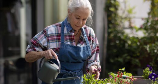 A senior woman waters flowers with a watering can on her patio