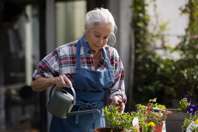 A senior woman waters flowers with a watering can on her patio