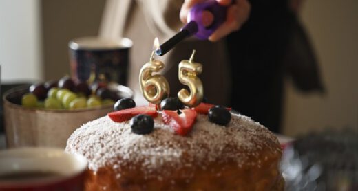 A festive close-up image capturing the moment candles are being lit on a birthday cake celebrating a 65th birthday.