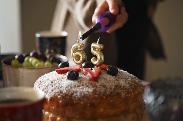 A festive close-up image capturing the moment candles are being lit on a birthday cake celebrating a 65th birthday.